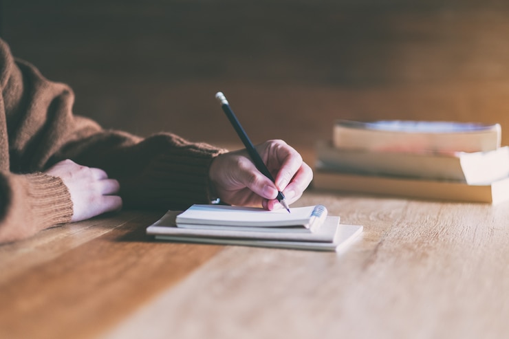 Photo woman writing on blank notebook on wooden table