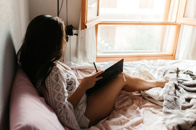 家でベッドに座って本を書いている女性