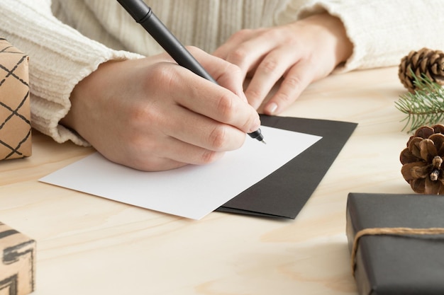 Photo woman writing a christmas card on a wooden table with christmas decoration