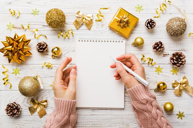 Photo woman writing christmas to do list on notebook on colored background with xmas decorations