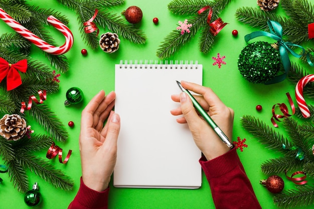 Woman writing Christmas to do list on notebook on colored background with xmas decorations