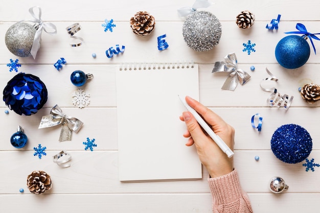 Woman writing Christmas to do list on notebook on colored background with xmas decorations