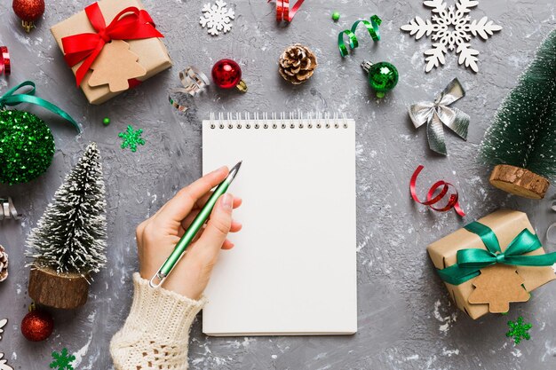 Woman writing Christmas to do list on notebook on colored background with xmas decorations