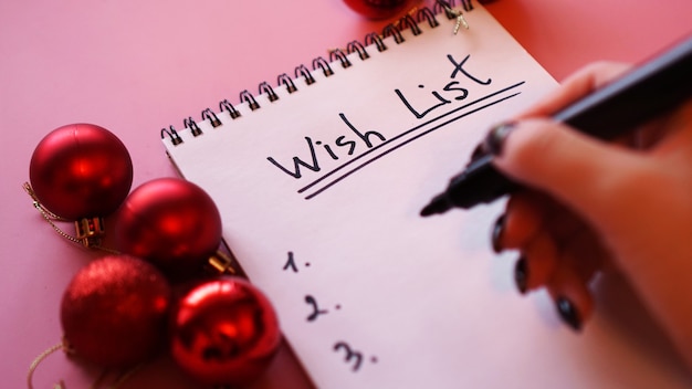 Woman writing her wish list. Festive design on pink background with Christmas red balls