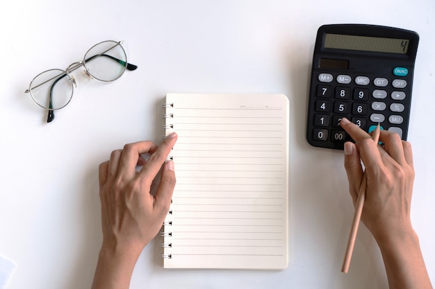 Woman writing on notebook while using calculator on desk