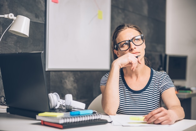 Woman writing notes and contemplating at the office