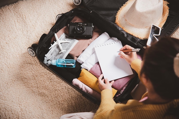 Woman writing paper take note and packing suitcase to vacation writing paper list sitting on room