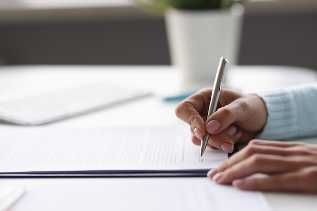 Woman writing with ballpoint pen in documents at table at home closeup remote work with papers