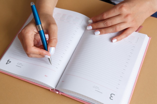 Woman writing with blue silver metal pen in pink diary