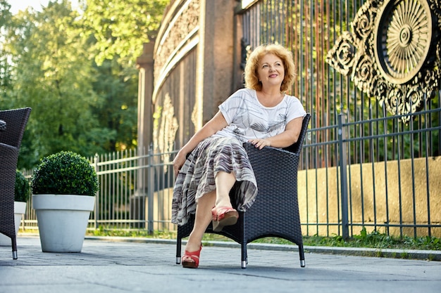 Женщина лет сидит в кресле возле кафе на тротуаре