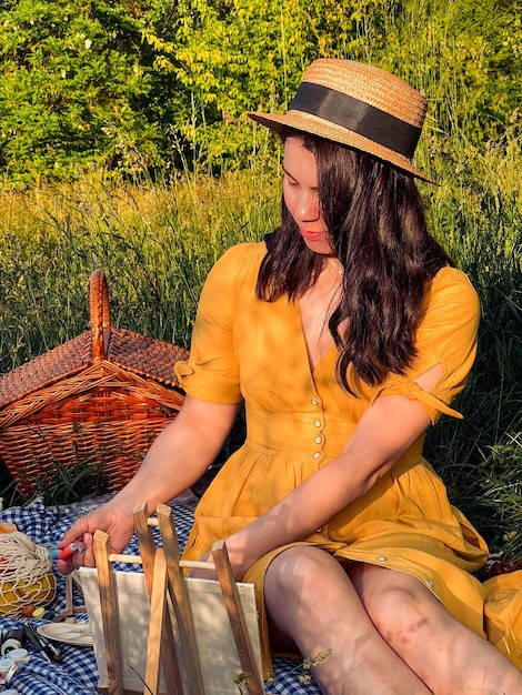 Woman in yellow dress and hat indulges in outdoor painting