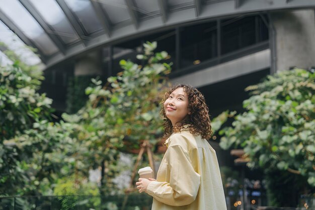 Photo a woman in a yellow dress is standing in front of a building with trees and plants