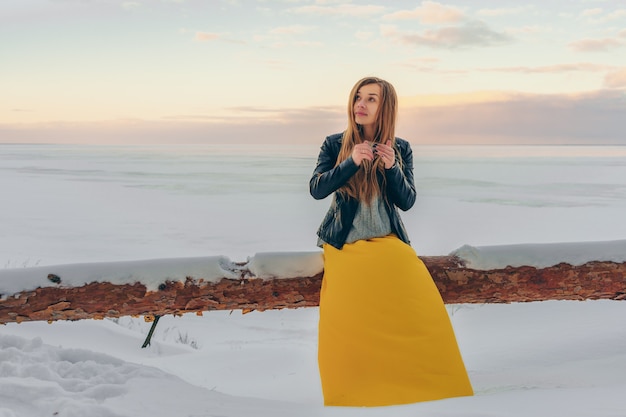 A woman in a yellow dress sits on a frozen lake in winter walking at sunset
