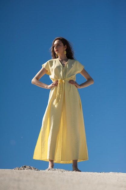 A woman in a yellow dress stands in front of a blue sky.