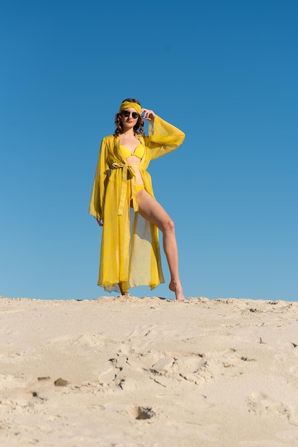 A woman in a yellow dress stands in the sand and poses for a photo