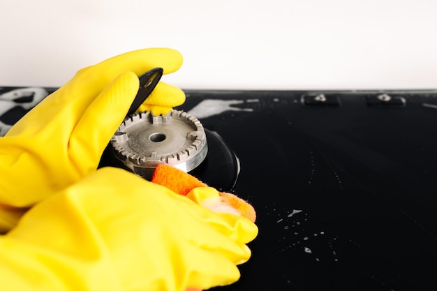 A woman in yellow gloves is cleaning the surface of a gas stove a sponge and detergent are used