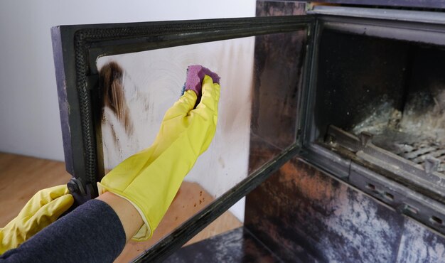 A woman in yellow gloves washes the glass of the fireplace Homework daily winter routine