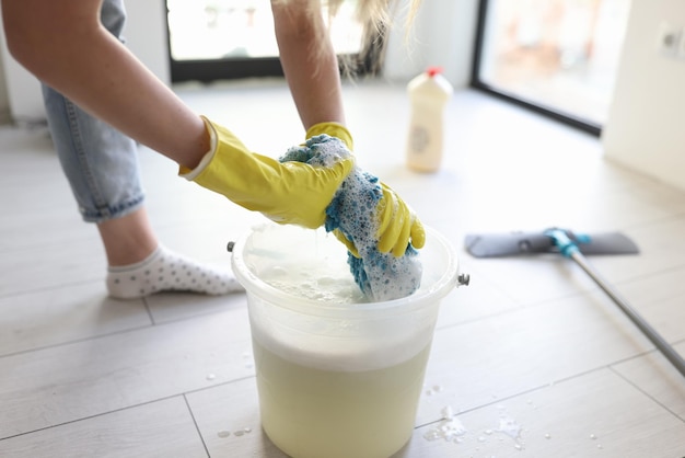 Woman in yellow gloves wrings mop rag over bucket in room housewife cleans parquet floor at