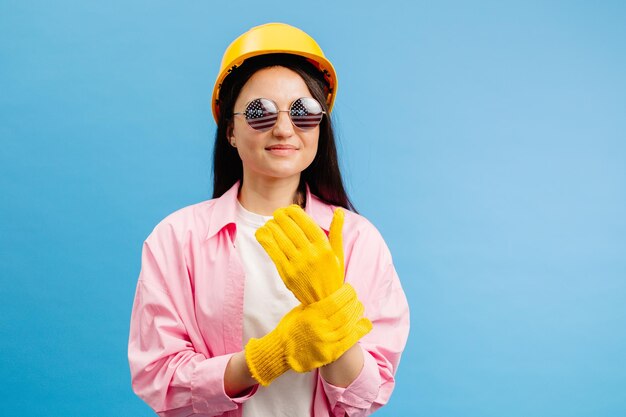 Woman in yellow helmet and gloves pointing and gesturing against blue studio background