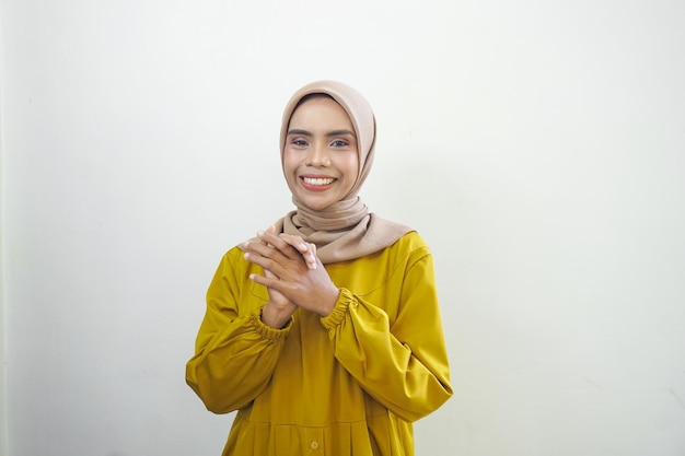 A woman in a yellow hijab stands in front of a white wall.