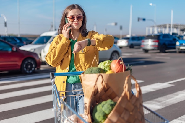 Woman in yellow jacket talking on smartphone and looking time on watch