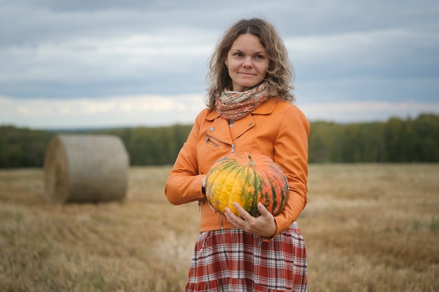 woman in a yellow leather jacket holds an orange pumpkin