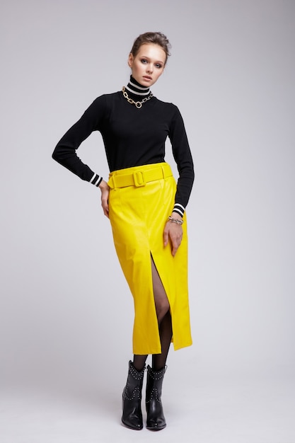 Woman in yellow leather skirt black blouse accessories boots on white background Studio Shot