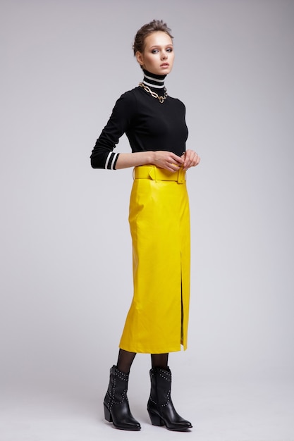 Woman in yellow leather skirt black blouse accessories boots on white background Studio Shot