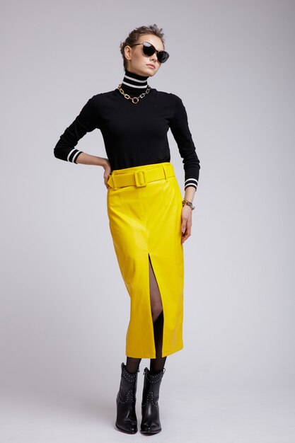 Woman in yellow leather skirt black blouse accessories sunglasses on white background