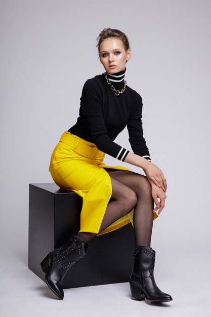 Woman in yellow leather skirt black blouse on white background Studio Shot Sitting at cube