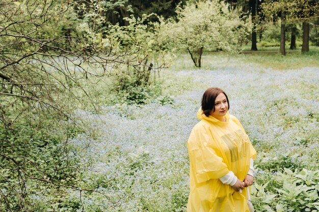 A woman in a yellow raincoat walks in the park and garden in the summer.