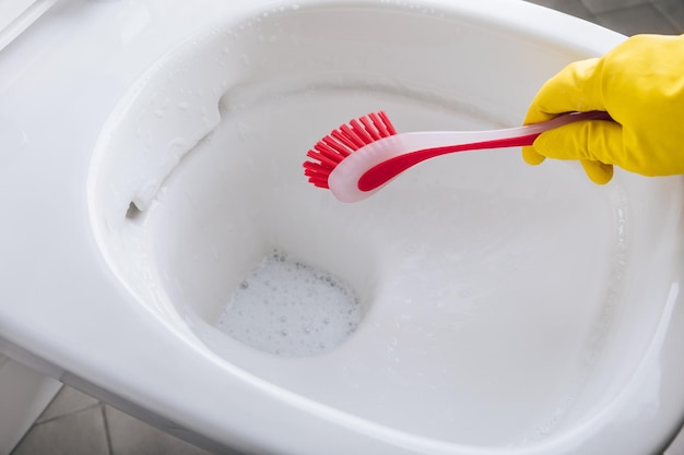 Woman in yellow rubber glove cleaning toilet bowl with red brush