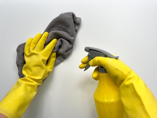 Foto una donna con guanti di gomma gialli pulisce la superficie usando un panno grigio e una bottiglia spray