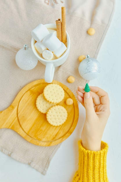 Woman in a yellow sweater holding a miniature Christmas tree with festive toys, coffee