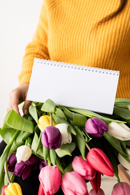 新鮮なピンクのチューリップと空白のカレンダーの花束と黄色のセーターの女性