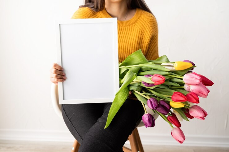 Photo woman in yellow sweater with bouquet of fresh pink tulips and blank frame