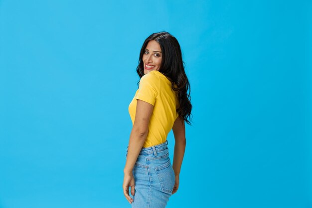 Woman in yellow t-shirt on blue background posing gestures emotions and signals with smile hands up