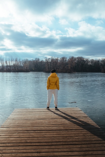 Woman in a yellow winter jacket against a river