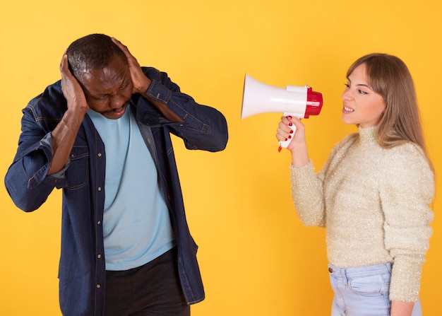 A woman yells at a man with an angry microphone, and a man covers his ears, 