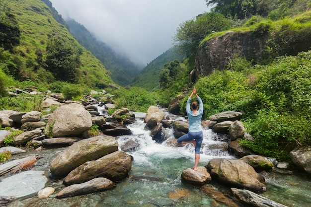 Женщина в позе дерева асаны Vrikshasana йоги на водопаде на открытом воздухе