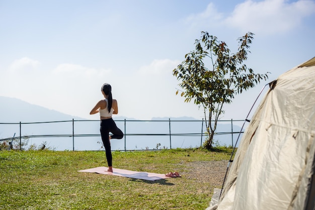 캠핑 텐트 와 함께 캠핑 장소 에서 요가 운동 을 하는 여자