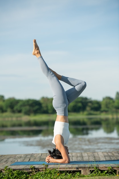 공원에서 휴식을 요가 매트에 여자. 요가 연습, headstand 운동을 하 고, 운동, 운동복, 바지와 탑을 입고 젊은 스포티 한 아시아 여자.