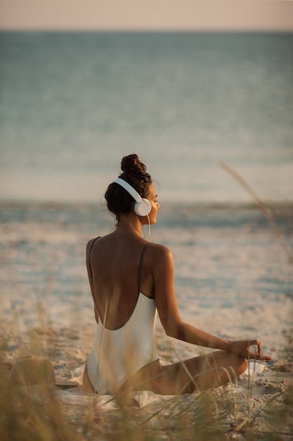 Woman in Yoga Meditation Pose with Headphones on the Beach