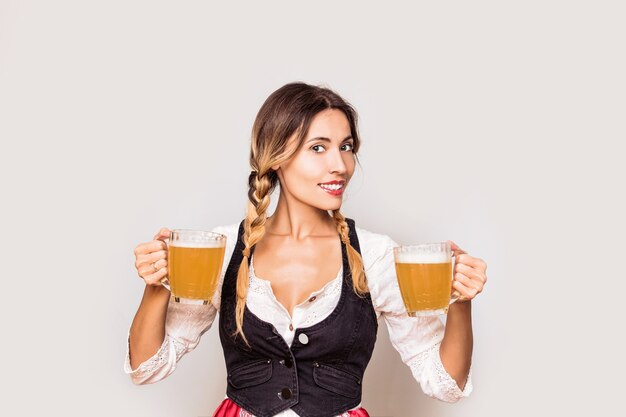 Woman young adult with beer mugs in his hands in a vest and white blouse clothes to Oktoberfest in the Studio