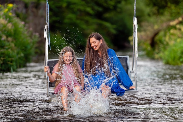 A woman and a young girl are swinging across a fastflowing river laughing and splashing with water