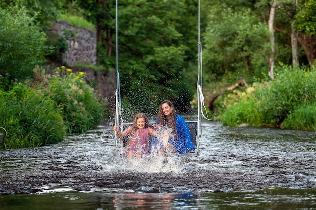 한 여자와 어린 소녀가 물을 튀기며 웃으면서 빠르게 흐르는 강을 건너고 있다