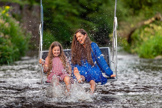 A woman and a young girl are swinging across a fastflowing river laughing and splashing with water