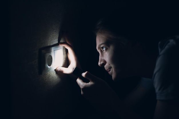 Фото Молодая женщина с фонариком в руке в темноте отключает домашнее электричество и меняет лампочку