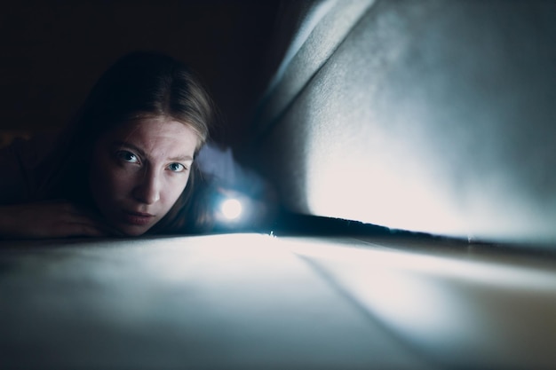 Woman young holding hand flashlight looking for dirt under furniture