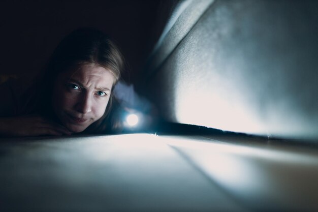 Photo woman young holding hand flashlight looking for dirt under furniture